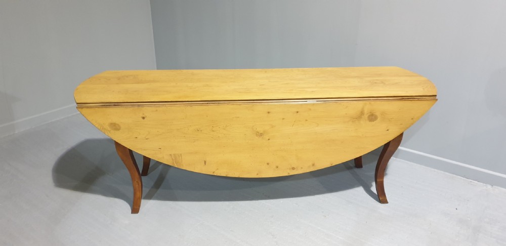 A large French farmhouse dining table featuring a light pine oval top supported by dark fruitwood cabriole legs. View VI