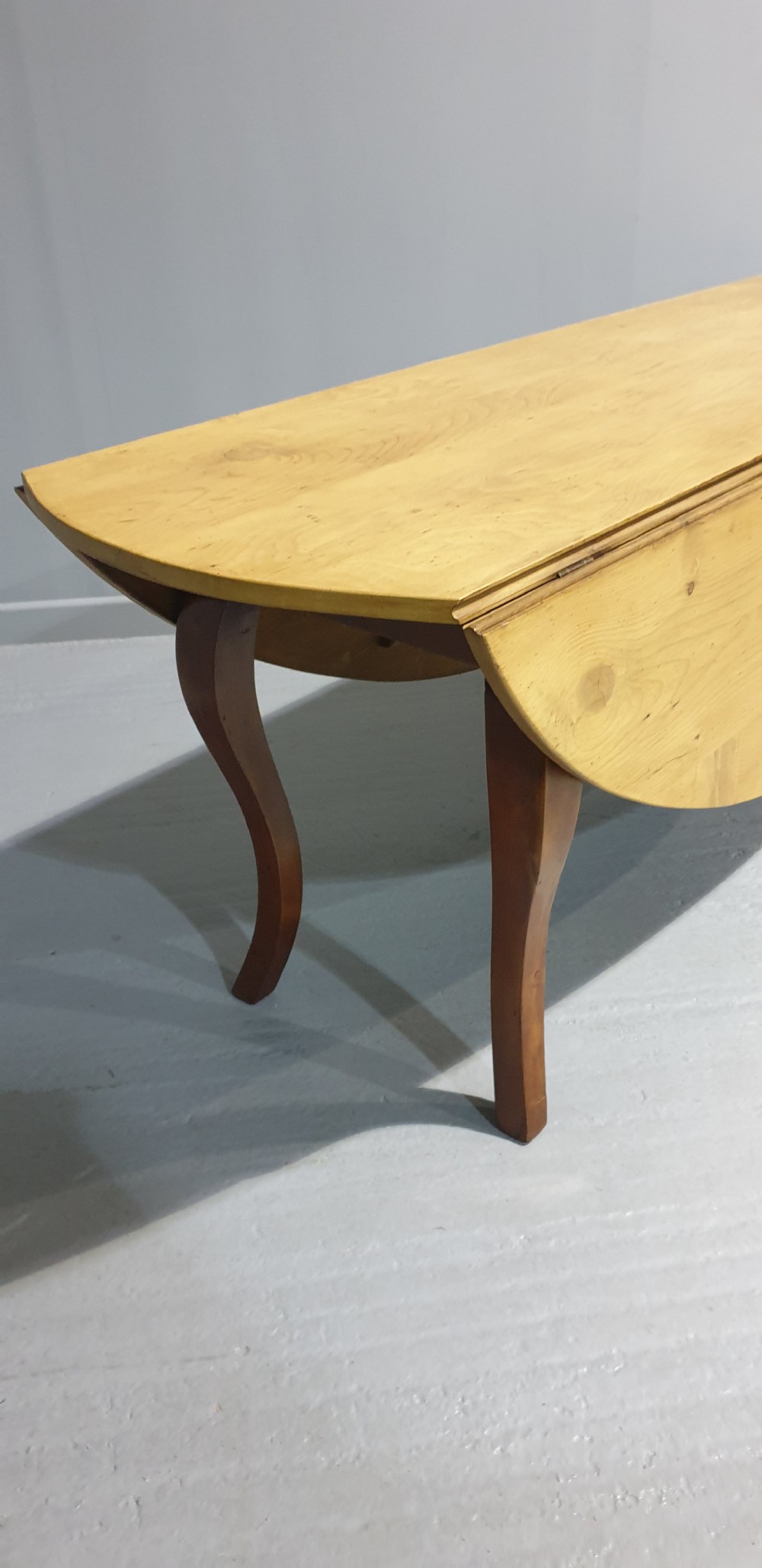A large French farmhouse dining table featuring a light pine oval top supported by dark fruitwood cabriole legs. View VII