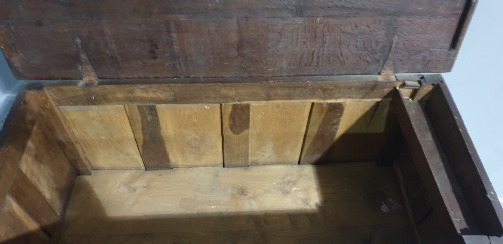 A 17th-century dark oak mule chest featuring four recessed front panels, a bottom drawer with brass knobs, central brass escutcheons, and turned bun feet. View V
