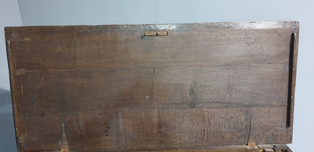 A 17th-century dark oak mule chest featuring four recessed front panels, a bottom drawer with brass knobs, central brass escutcheons, and turned bun feet. View VI