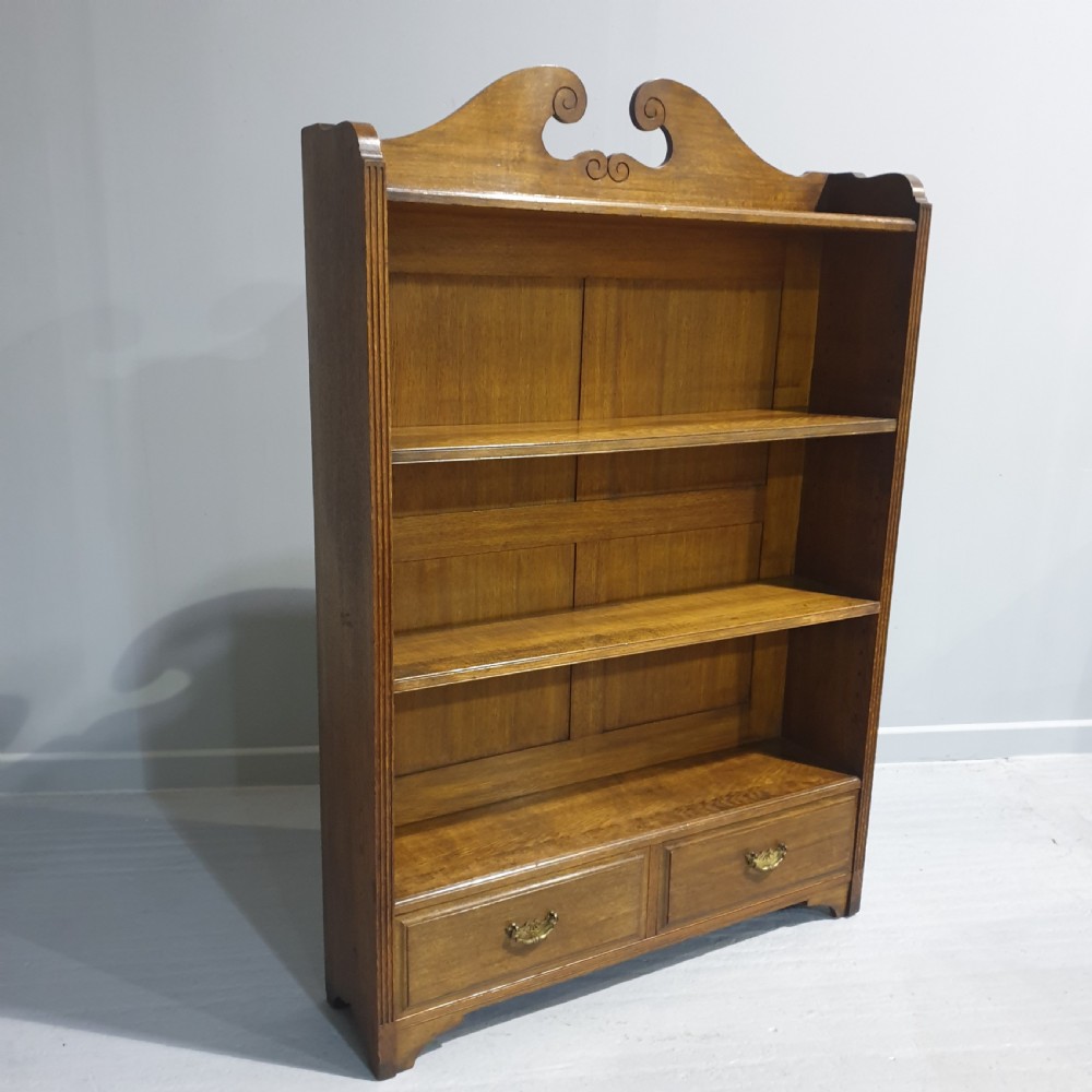 A Victorian medium brown oak open bookcase featuring a carved scroll pediment, adjustable shelves, and two drawers at the base with brass handles. View II