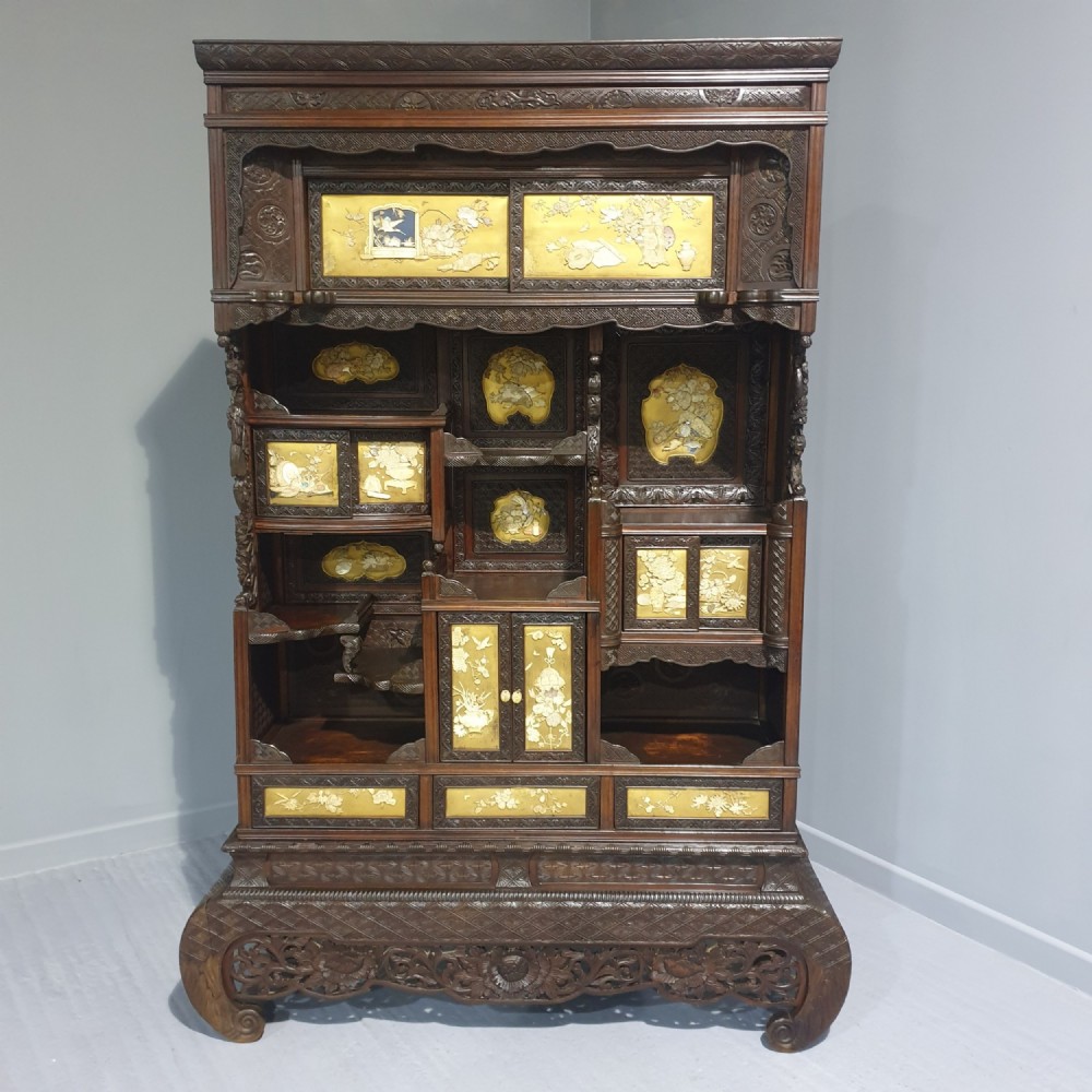 An intricately carved dark wood Japanese Meiji period Shibayama cabinet featuring multi-tiered asymmetrical shelves and gold lacquer panels inset with shell and bone motifs.