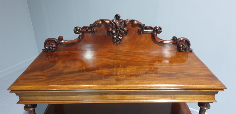 A Victorian mahogany buffet server featuring a carved scroll splashback, turned columns, a two-door lower cupboard, and brass castors. View V
