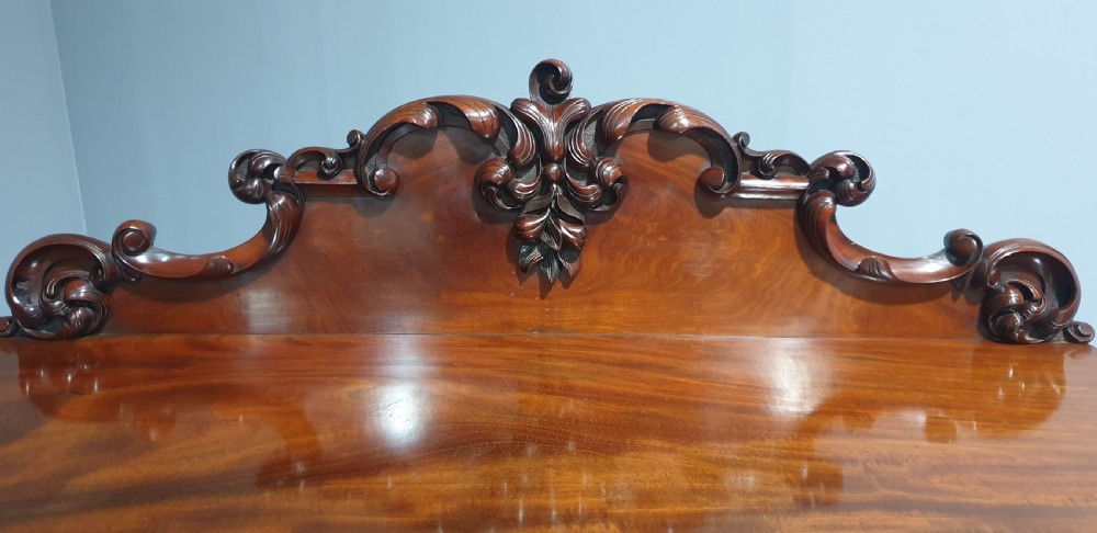 A Victorian mahogany buffet server featuring a carved scroll splashback, turned columns, a two-door lower cupboard, and brass castors. View VI