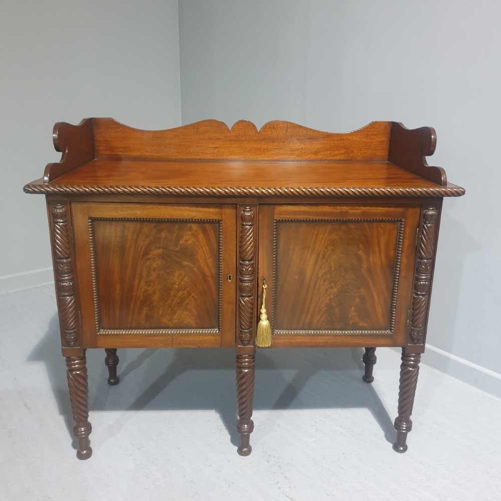 A mahogany Regency sideboard featuring a shaped splashback, rope-twist carved details, and flame mahogany panelled doors supported by spiral-turned legs.