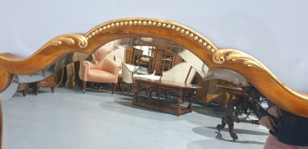 A shaped walnut overmantel mirror featuring gilded beaded borders and leaf accents framing a large central plate. View V