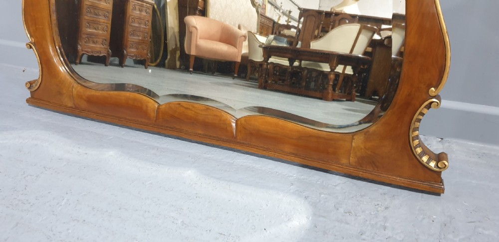 A shaped walnut overmantel mirror featuring gilded beaded borders and leaf accents framing a large central plate. View VII