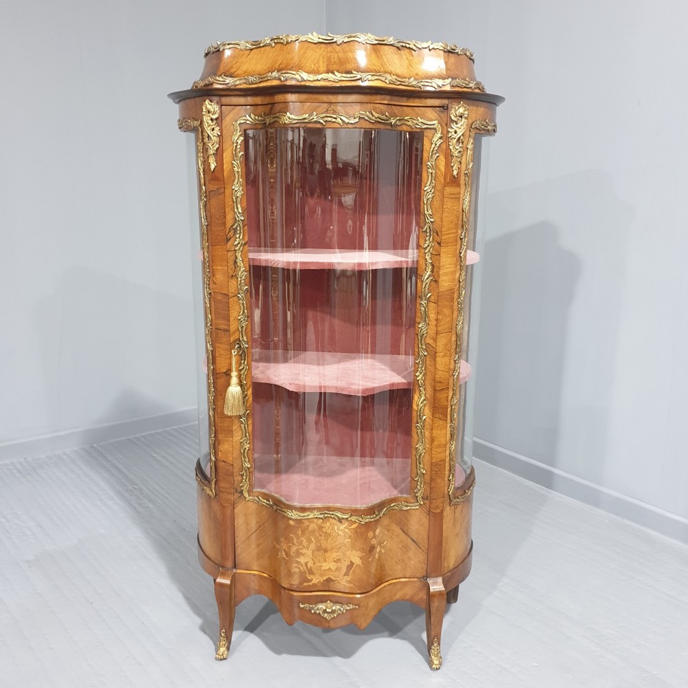 An antique French Louis XV style glazed vitrine display cabinet featuring curved glass sides, floral marquetry inlay, and detailed ormolu mounts.