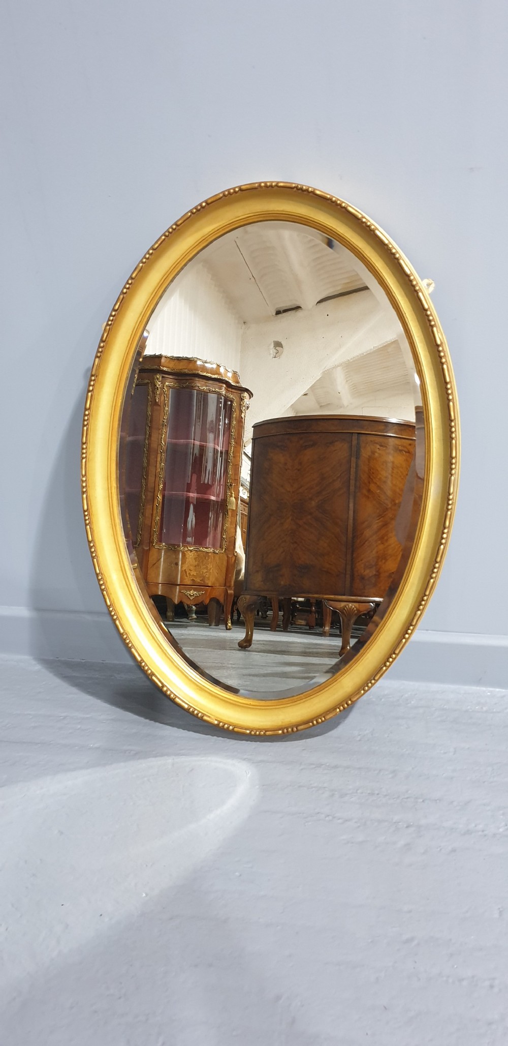 An oval Victorian wall mirror featuring a moulded gold gilt frame with subtle beaded detailing around the inner rim.