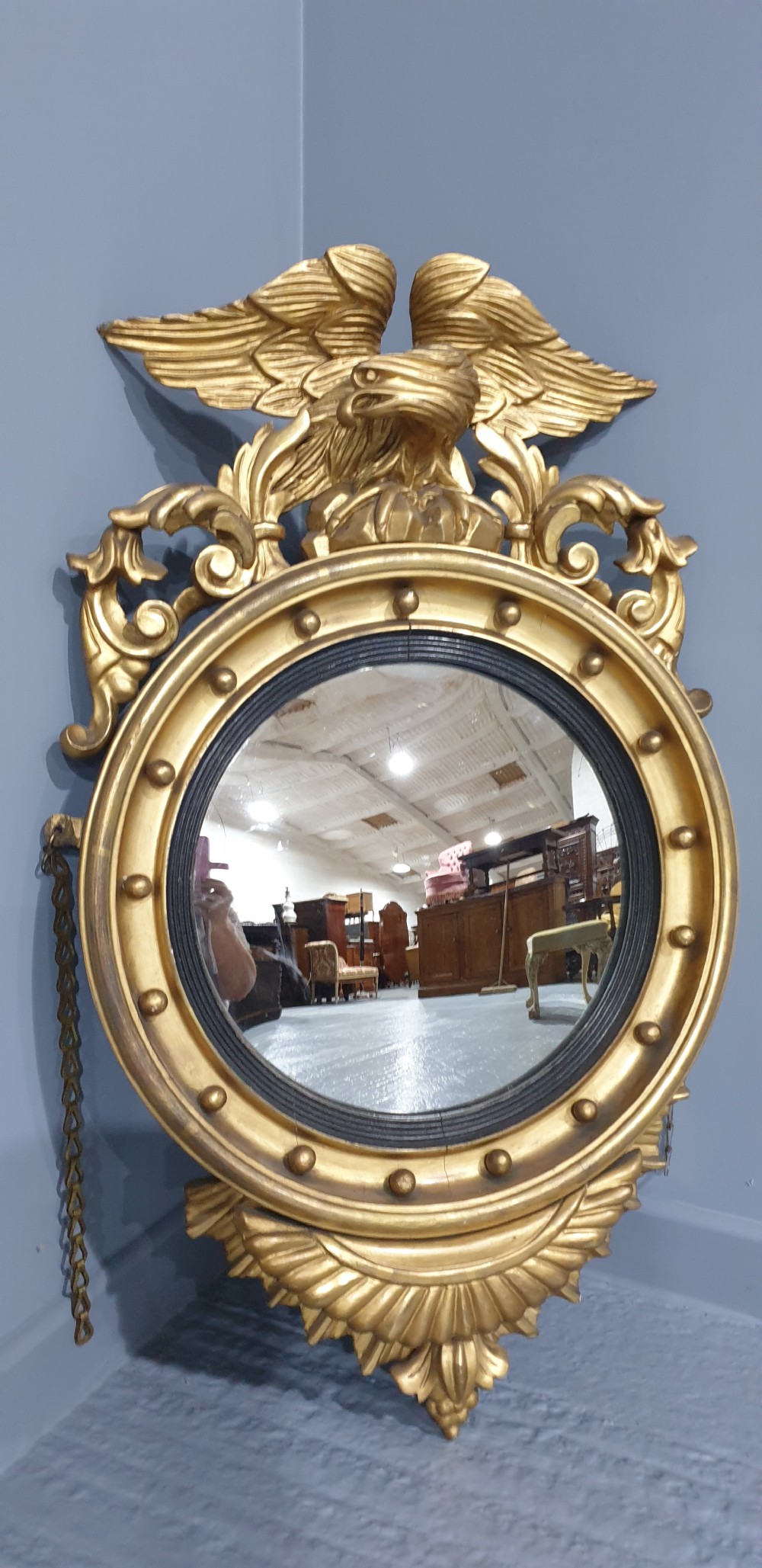 An antique Regency giltwood convex wall mirror featuring a carved eagle cresting, ball-studded circular frame, and acanthus apron. View II