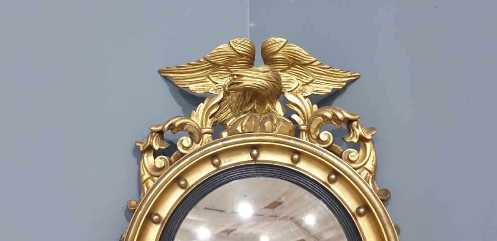 An antique Regency giltwood convex wall mirror featuring a carved eagle cresting, ball-studded circular frame, and acanthus apron. View IV