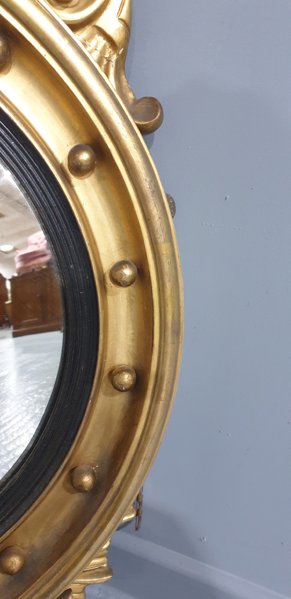An antique Regency giltwood convex wall mirror featuring a carved eagle cresting, ball-studded circular frame, and acanthus apron. View VII