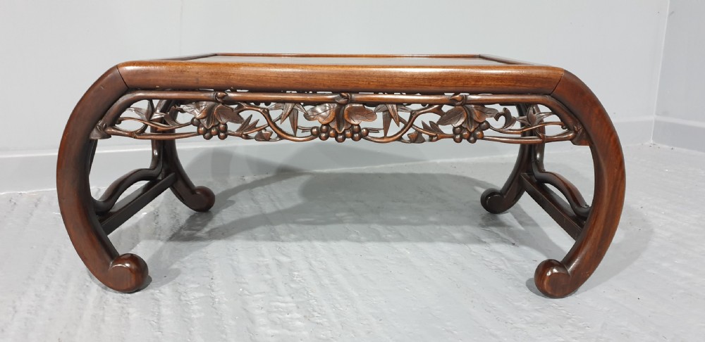A low warm brown carved hardwood Chinese Kang opium table featuring curved legs and pierced floral carvings along the apron. View II