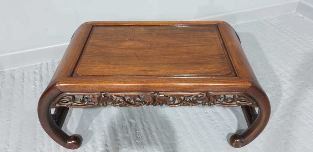 A low warm brown carved hardwood Chinese Kang opium table featuring curved legs and pierced floral carvings along the apron. View III