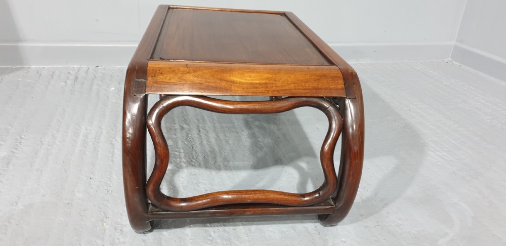 A low warm brown carved hardwood Chinese Kang opium table featuring curved legs and pierced floral carvings along the apron. View V