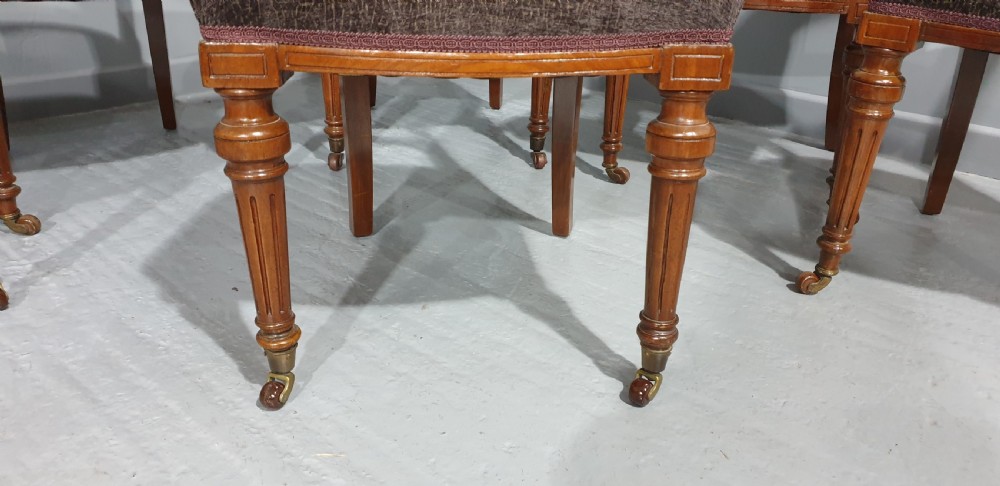 A set of six Victorian carved walnut dining chairs featuring open curved backrests, brown textured fabric seats, and turned front legs fitted with brass castors. View III