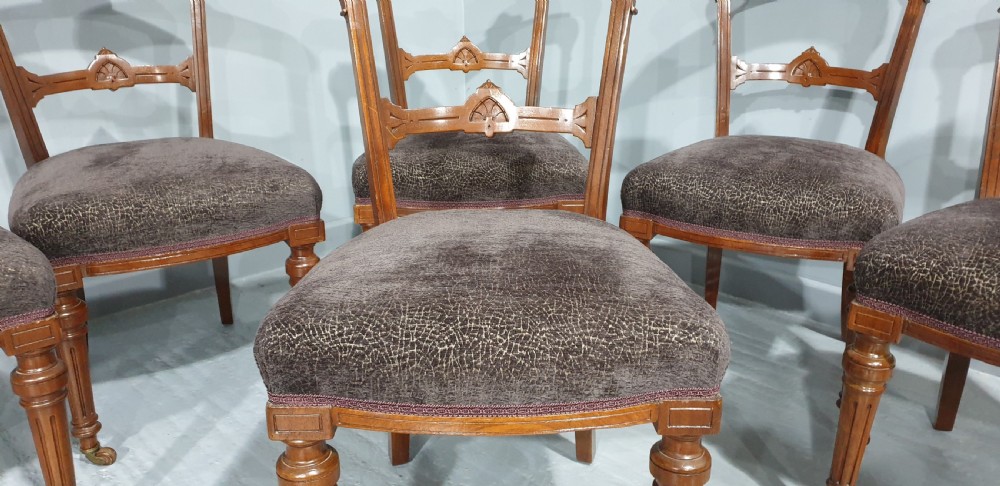 A set of six Victorian carved walnut dining chairs featuring open curved backrests, brown textured fabric seats, and turned front legs fitted with brass castors. View IV