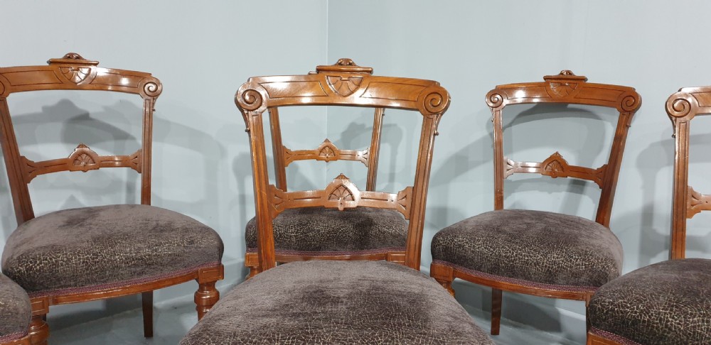 A set of six Victorian carved walnut dining chairs featuring open curved backrests, brown textured fabric seats, and turned front legs fitted with brass castors. View VI