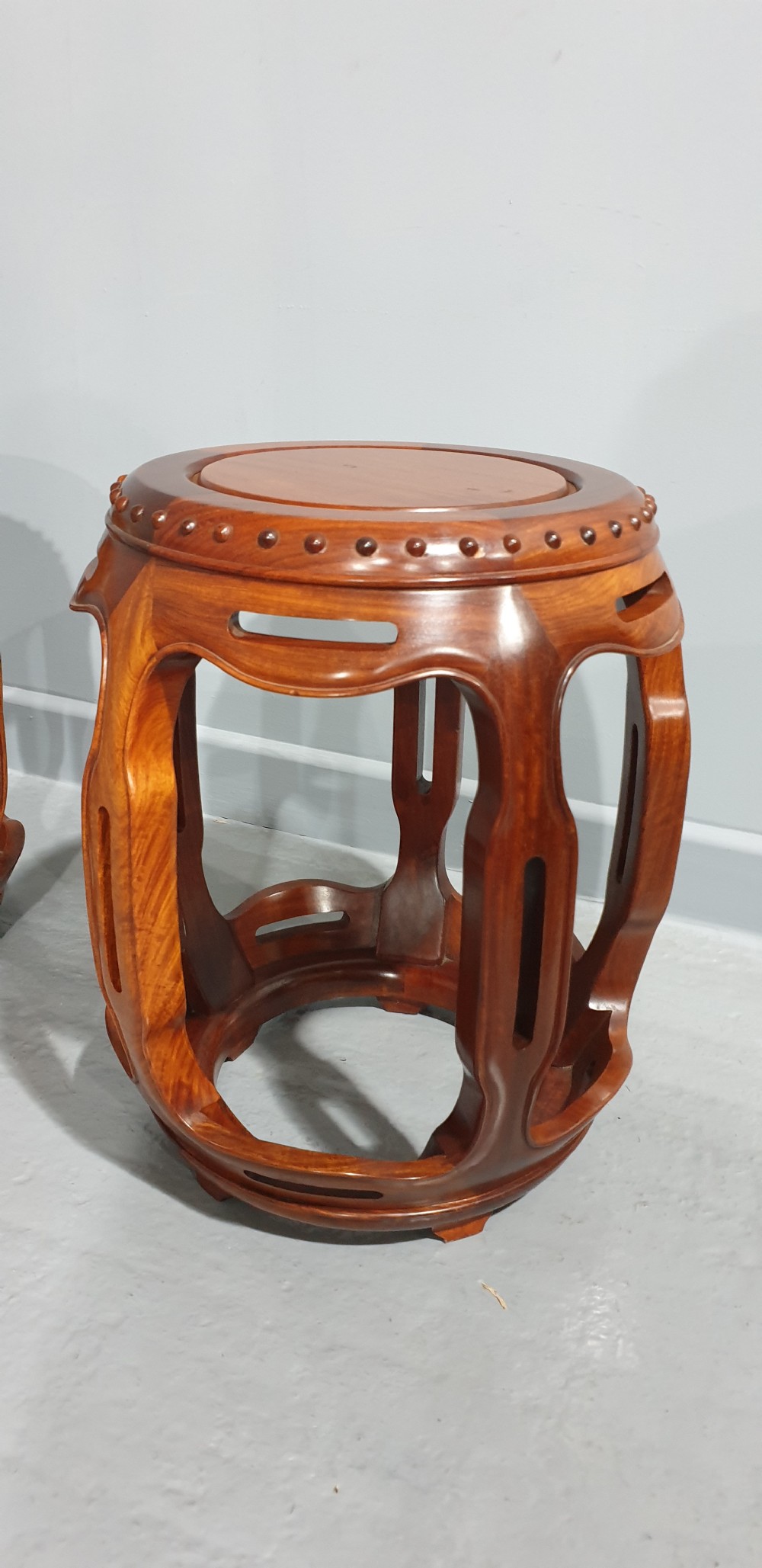 A pair of warm brown carved teak barrel stools featuring openwork sides and carved stud details along the circular top rim. View II