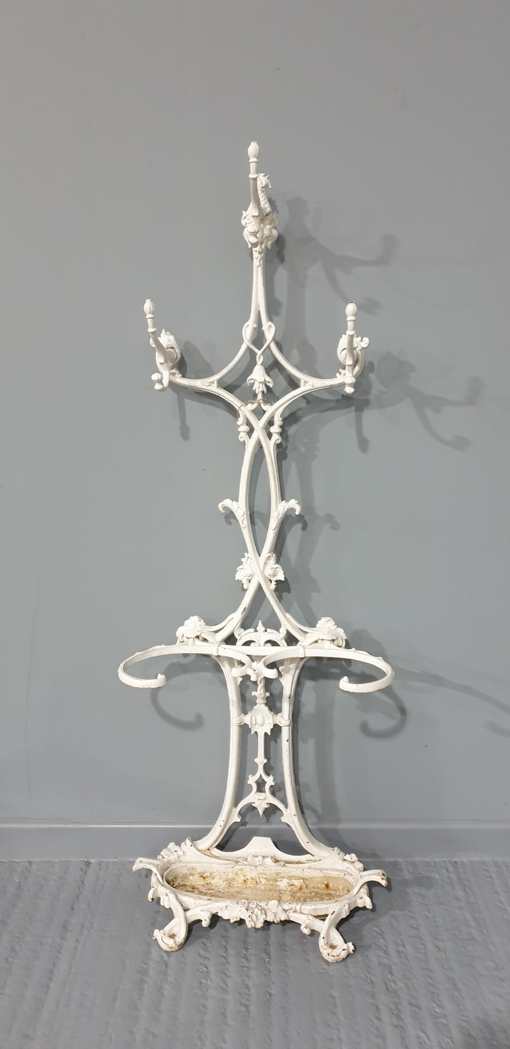 An ornate white painted cast iron hall stand featuring multiple coat hooks, scrollwork frame, umbrella support rings, and an integrated drip tray at the base. View II