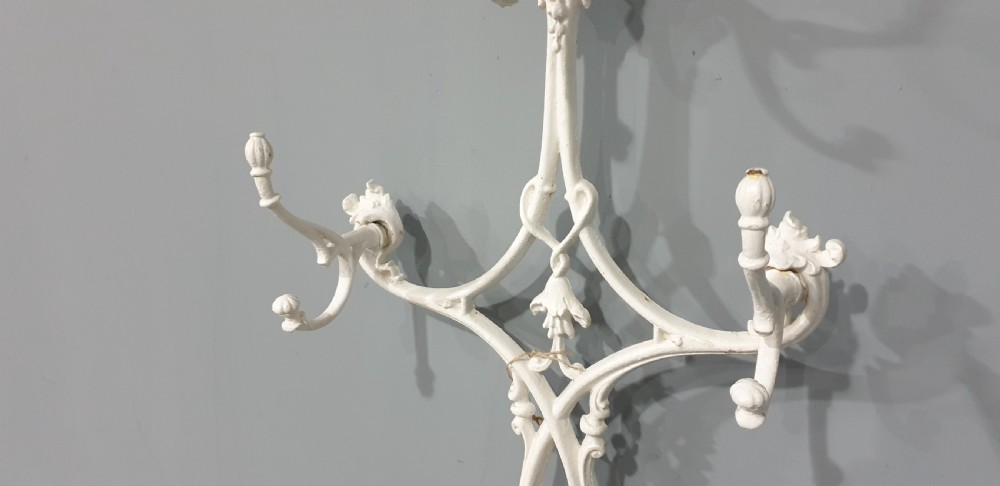 An ornate white painted cast iron hall stand featuring multiple coat hooks, scrollwork frame, umbrella support rings, and an integrated drip tray at the base. View V