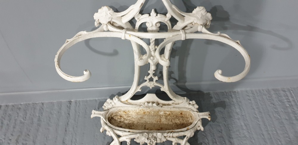 An ornate white painted cast iron hall stand featuring multiple coat hooks, scrollwork frame, umbrella support rings, and an integrated drip tray at the base. View VII