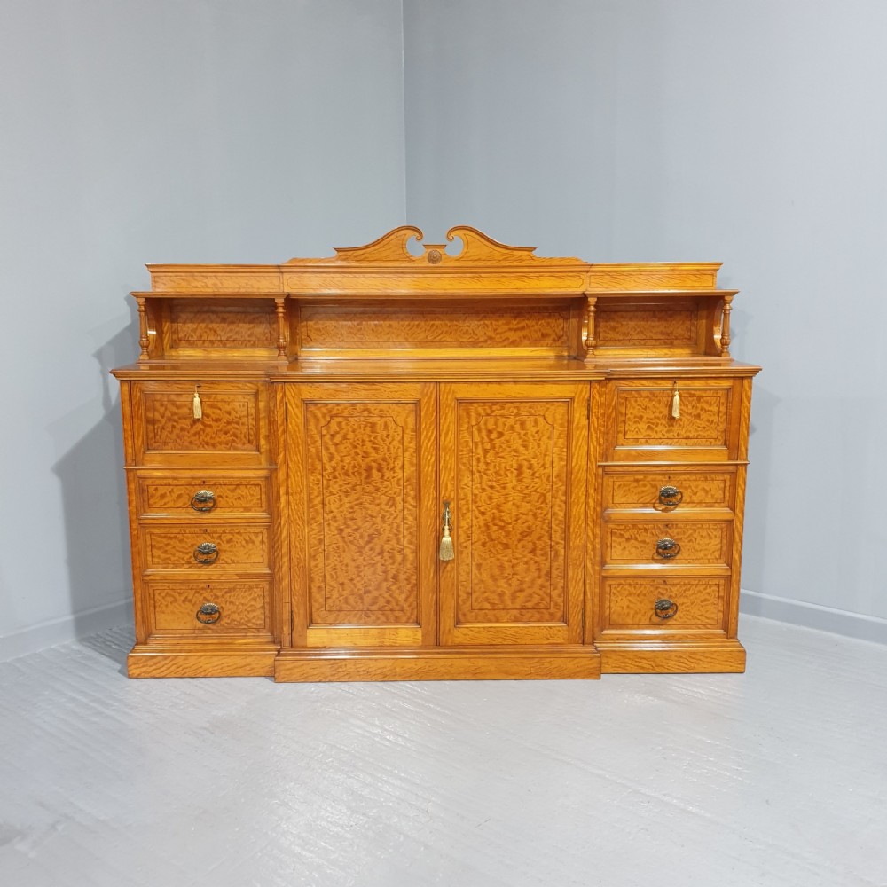 A Victorian satinwood low press cabinet featuring central panelled double doors, flanking drawer stacks, brass drop handles, and an upper scroll gallery.