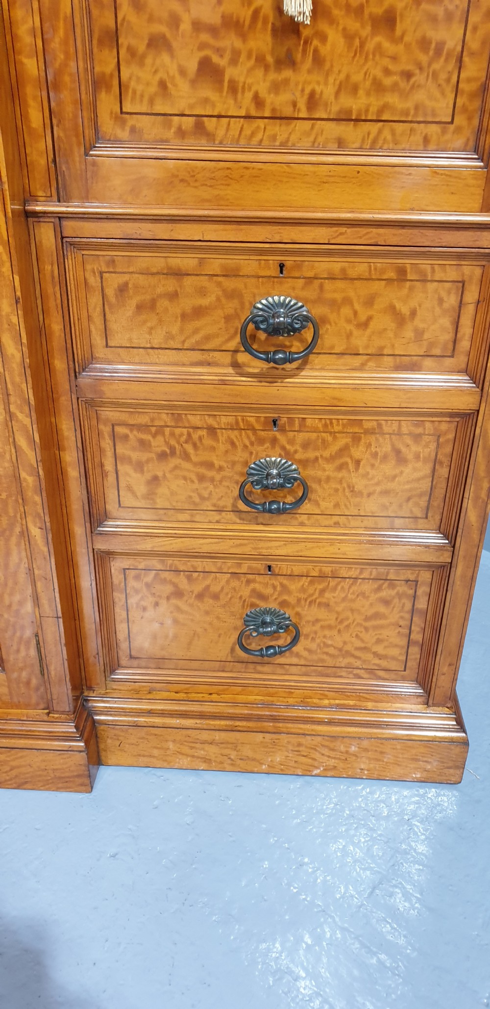 A Victorian satinwood low press cabinet featuring central panelled double doors, flanking drawer stacks, brass drop handles, and an upper scroll gallery. View III