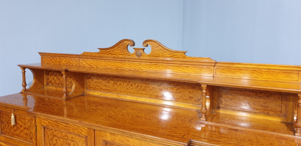 A Victorian satinwood low press cabinet featuring central panelled double doors, flanking drawer stacks, brass drop handles, and an upper scroll gallery. View V