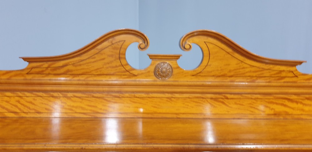 A Victorian satinwood low press cabinet featuring central panelled double doors, flanking drawer stacks, brass drop handles, and an upper scroll gallery. View VI