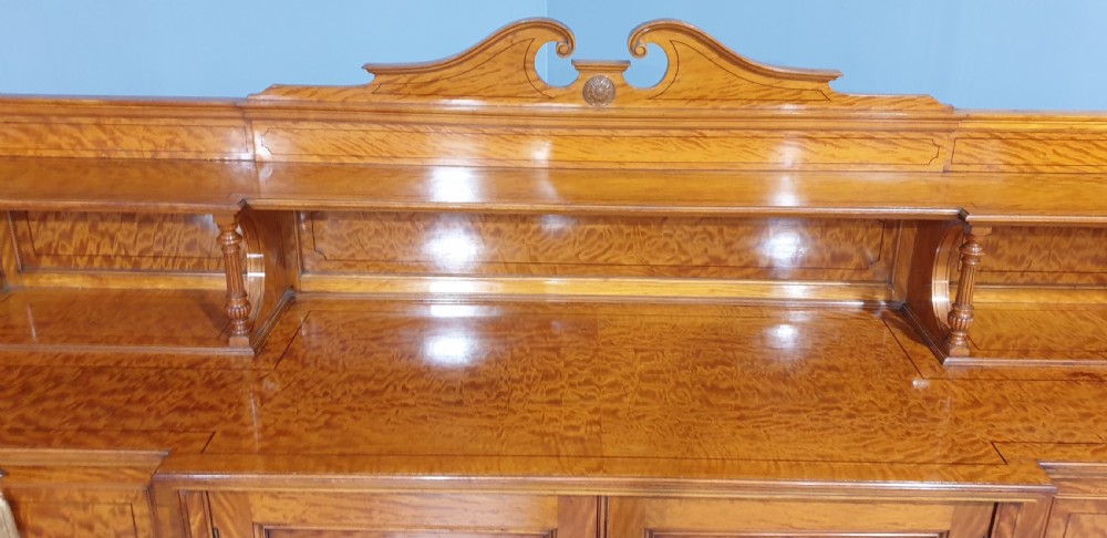 A Victorian satinwood low press cabinet featuring central panelled double doors, flanking drawer stacks, brass drop handles, and an upper scroll gallery. View VII