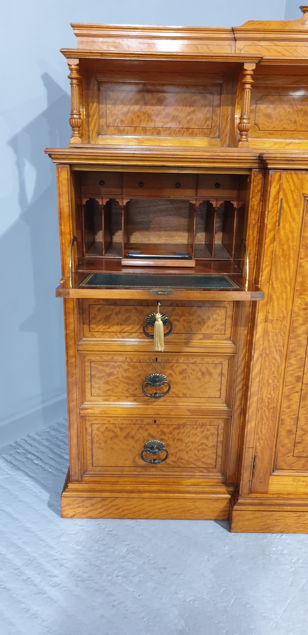 A Victorian satinwood low press cabinet featuring central panelled double doors, flanking drawer stacks, brass drop handles, and an upper scroll gallery. View VIII