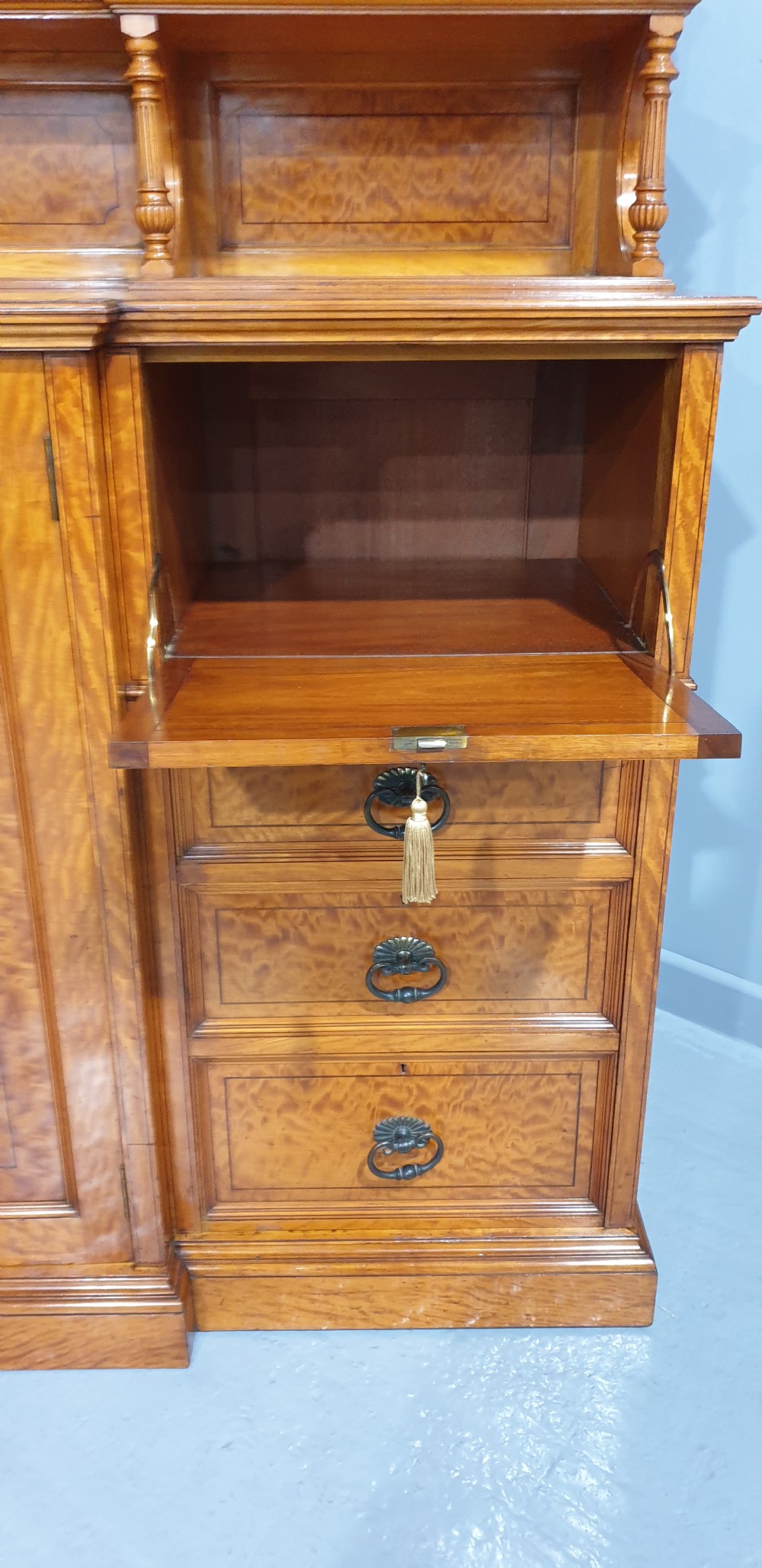 A Victorian satinwood low press cabinet featuring central panelled double doors, flanking drawer stacks, brass drop handles, and an upper scroll gallery. View IX