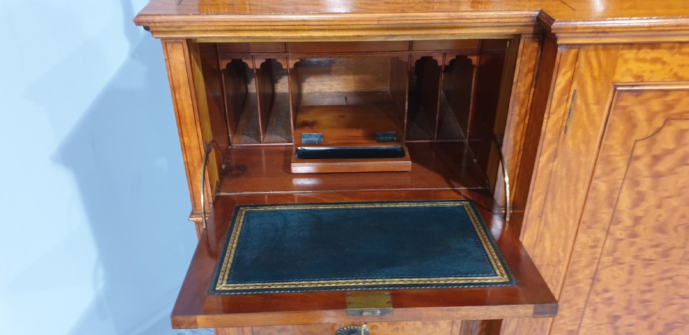A Victorian satinwood low press cabinet featuring central panelled double doors, flanking drawer stacks, brass drop handles, and an upper scroll gallery. View X