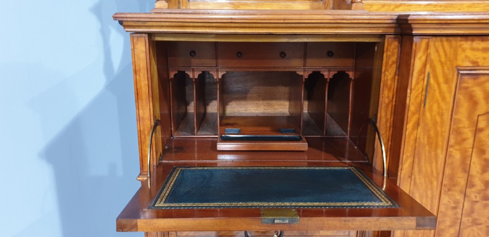 A Victorian satinwood low press cabinet featuring central panelled double doors, flanking drawer stacks, brass drop handles, and an upper scroll gallery. View XII