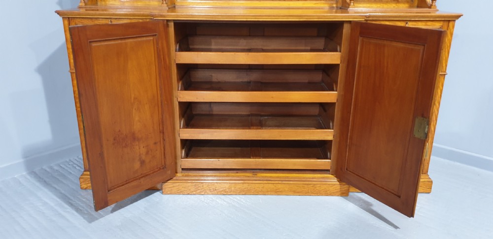 A Victorian satinwood low press cabinet featuring central panelled double doors, flanking drawer stacks, brass drop handles, and an upper scroll gallery. View XIII
