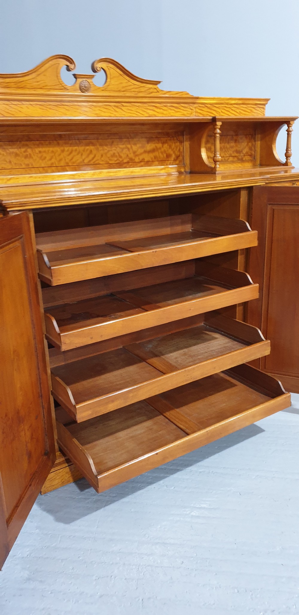 A Victorian satinwood low press cabinet featuring central panelled double doors, flanking drawer stacks, brass drop handles, and an upper scroll gallery. View XIV