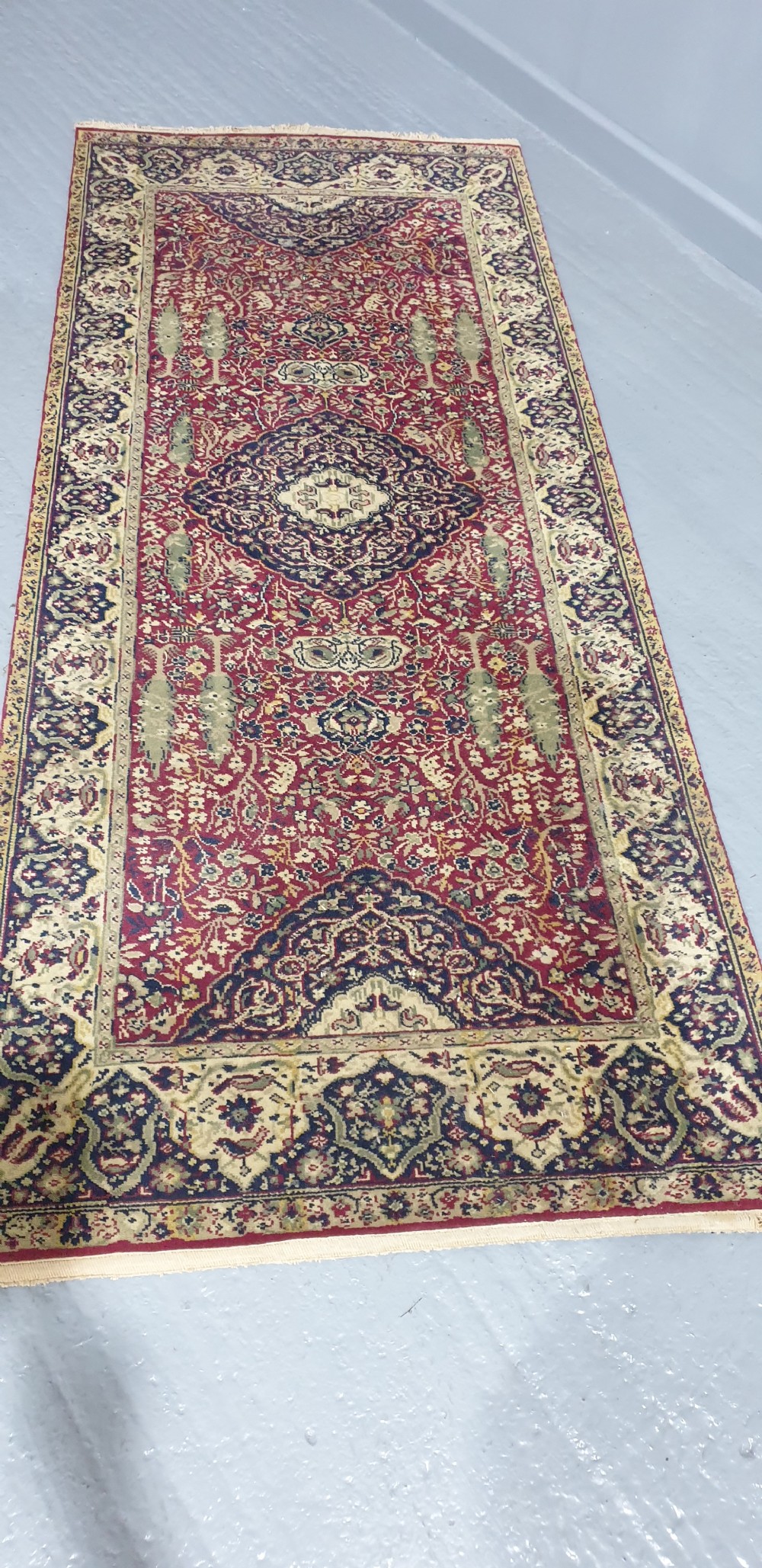 An elongated hand-knotted antique wool runner rug featuring a detailed central medallion and ornate floral motifs in deep red, navy blue, and cream colours. View II