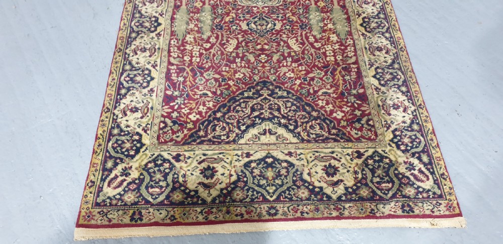 An elongated hand-knotted antique wool runner rug featuring a detailed central medallion and ornate floral motifs in deep red, navy blue, and cream colours. View III