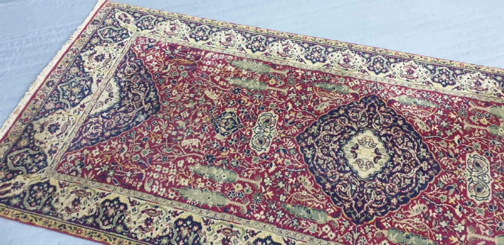 An elongated hand-knotted antique wool runner rug featuring a detailed central medallion and ornate floral motifs in deep red, navy blue, and cream colours. View VII
