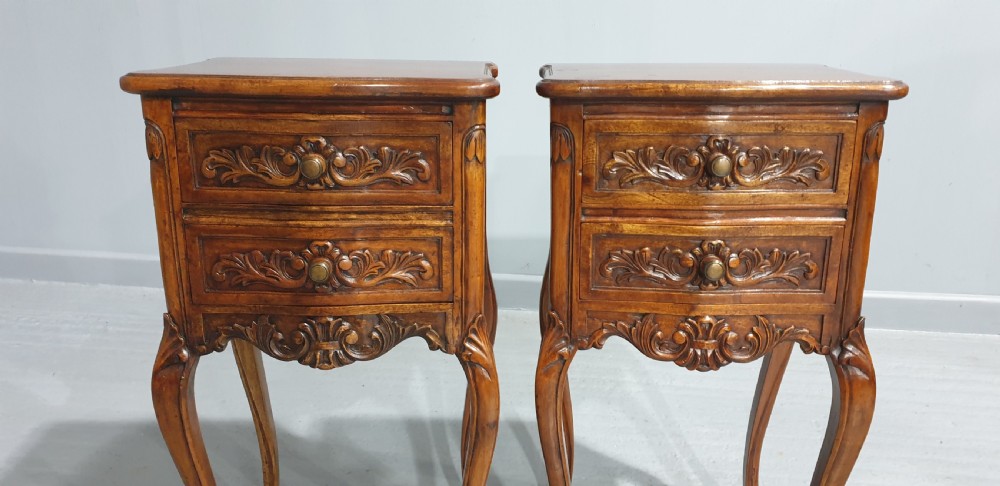 A pair of carved warm brown mahogany bedside tables featuring two drawers each, intricate foliate carvings, curved aprons, and slender cabriole legs. View II