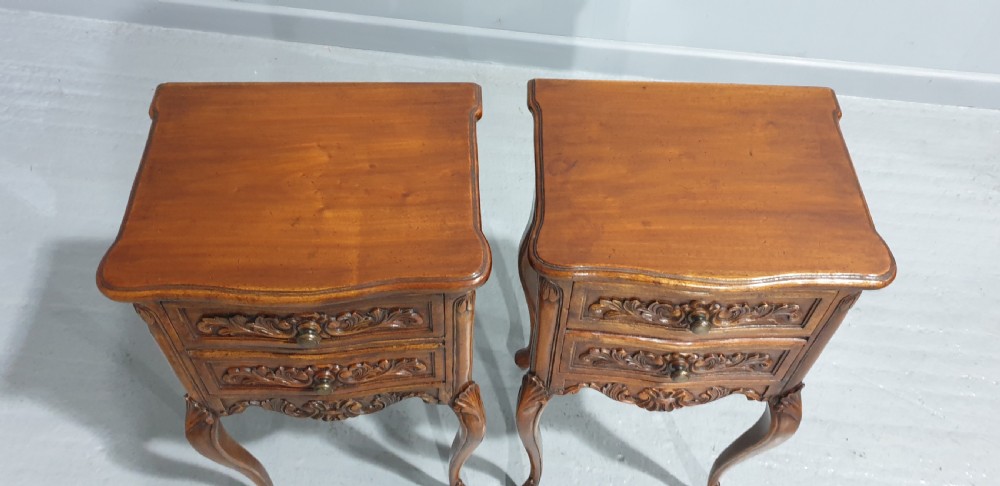 A pair of carved warm brown mahogany bedside tables featuring two drawers each, intricate foliate carvings, curved aprons, and slender cabriole legs. View V