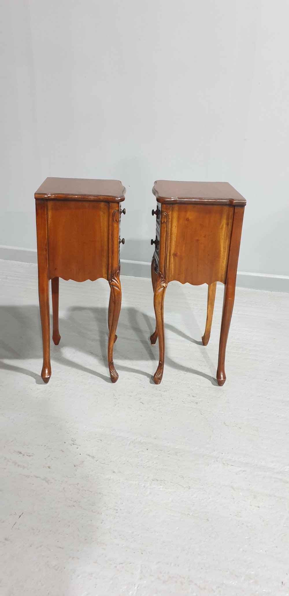 A pair of carved warm brown mahogany bedside tables featuring two drawers each, intricate foliate carvings, curved aprons, and slender cabriole legs. View VI