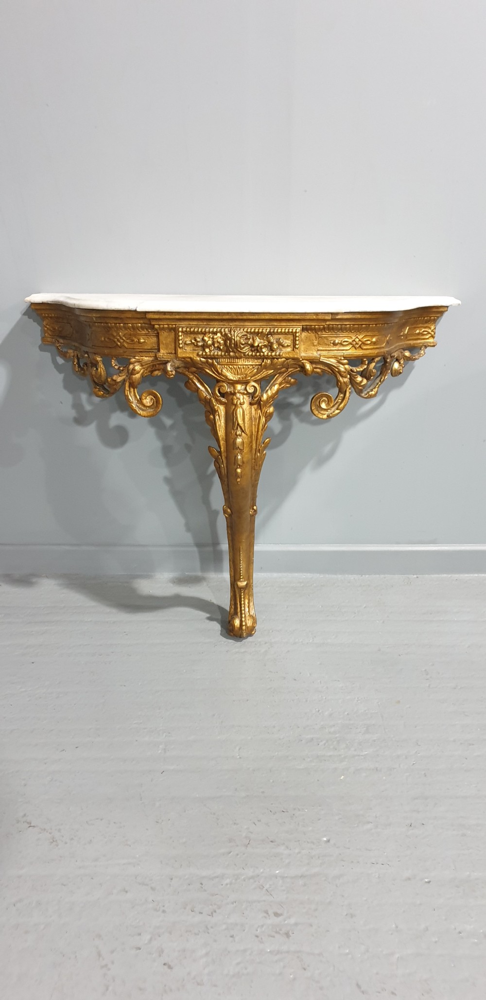 A 19th-century French giltwood wall-mounted console table featuring a single carved leg and a white marble top. View X
