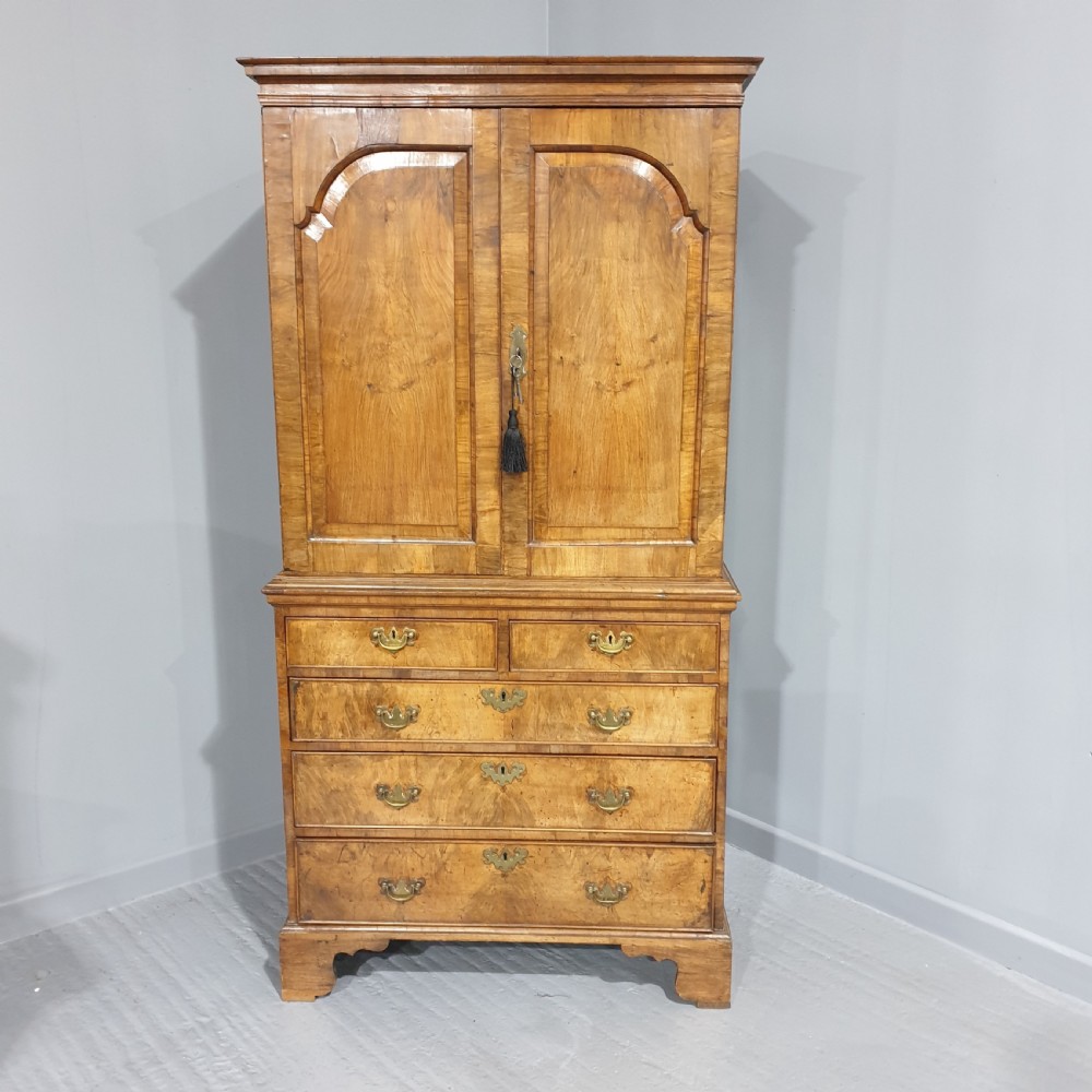 A George I walnut secretaire chest of small proportions featuring an upper double cabinet with arched door panels over a base of four drawers with brass hardware. View II
