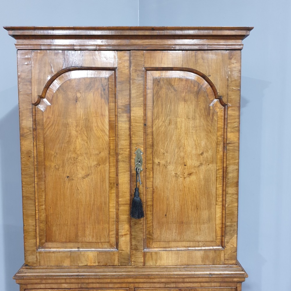 A George I walnut secretaire chest of small proportions featuring an upper double cabinet with arched door panels over a base of four drawers with brass hardware. View IV