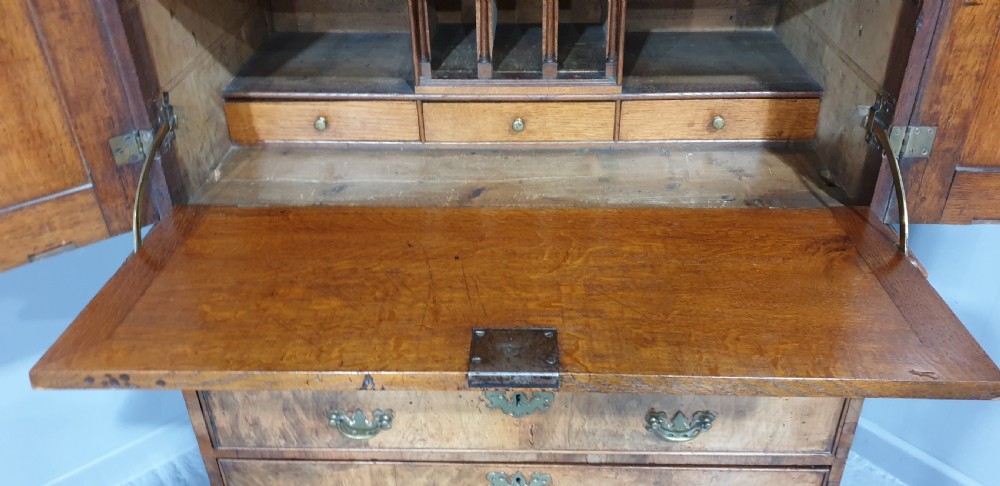 A George I walnut secretaire chest of small proportions featuring an upper double cabinet with arched door panels over a base of four drawers with brass hardware. View XV