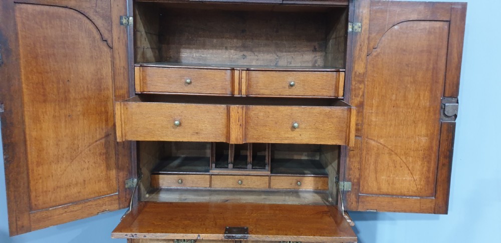 A George I walnut secretaire chest of small proportions featuring an upper double cabinet with arched door panels over a base of four drawers with brass hardware. View XVII