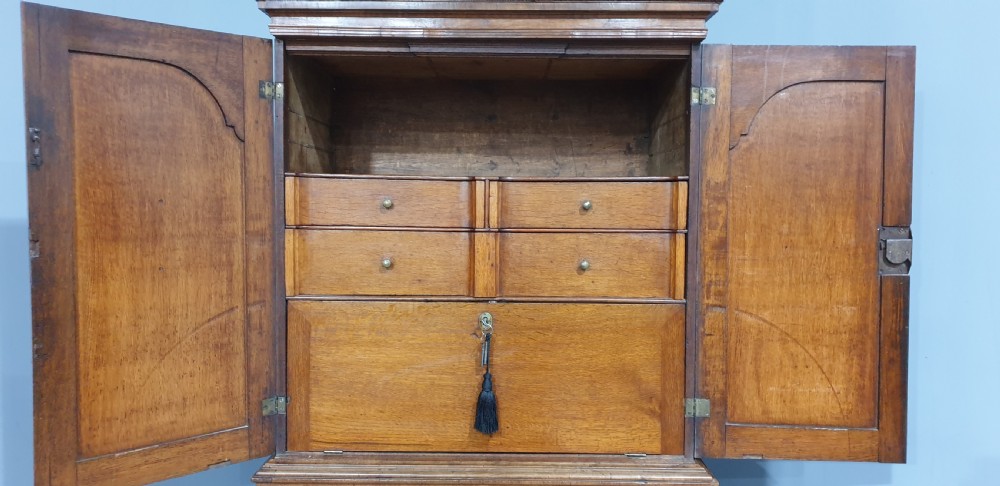 A George I walnut secretaire chest of small proportions featuring an upper double cabinet with arched door panels over a base of four drawers with brass hardware. View XIX