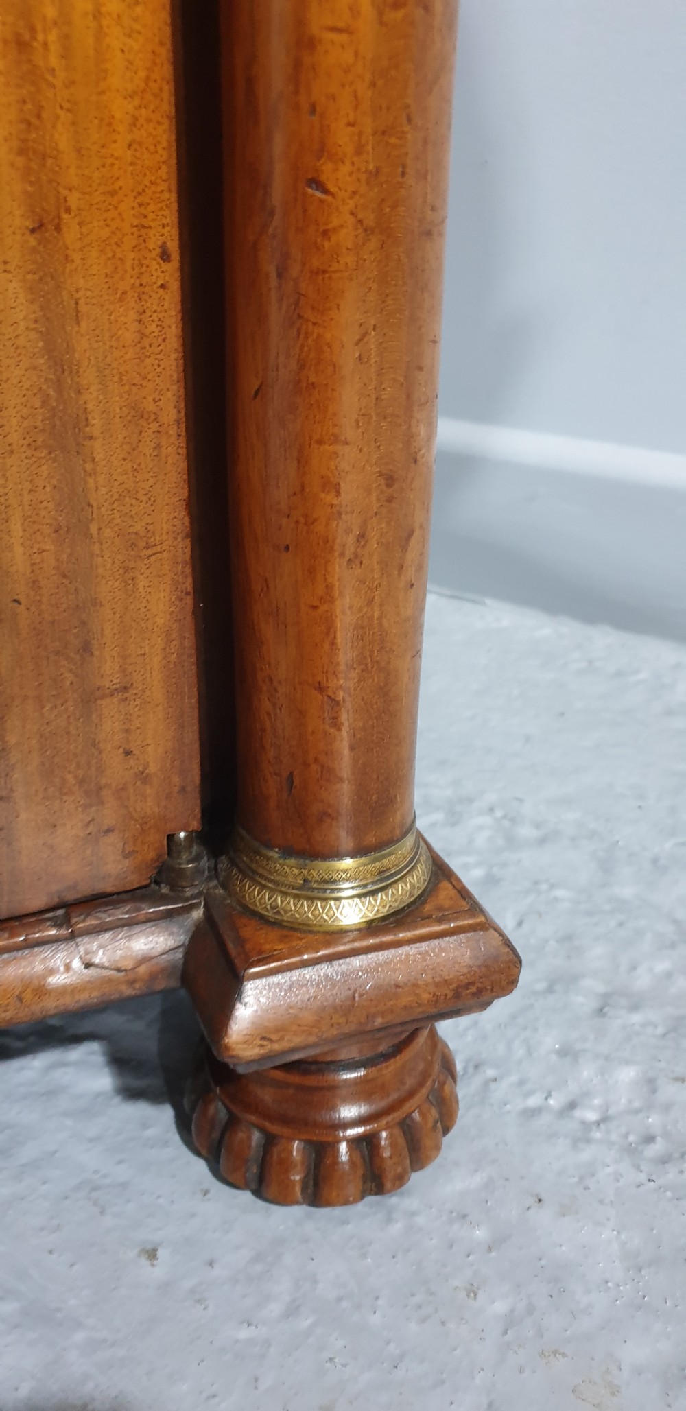 An antique Regency mahogany side cabinet featuring two top drawers over double doors with brass diamond grilles backed by green fabric, flanked by columns. View VII